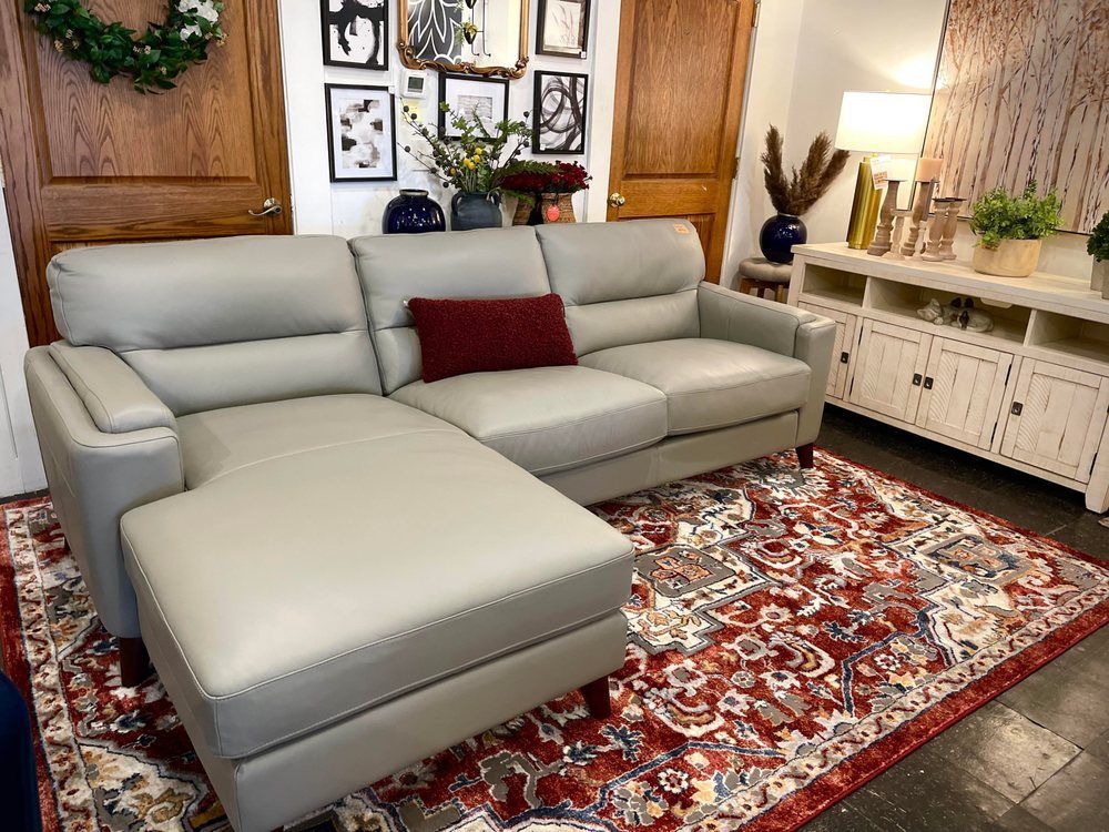 Gray leather sectional sofa with a red throw pillow on a patterned rug, in a room with art and a cabinet.