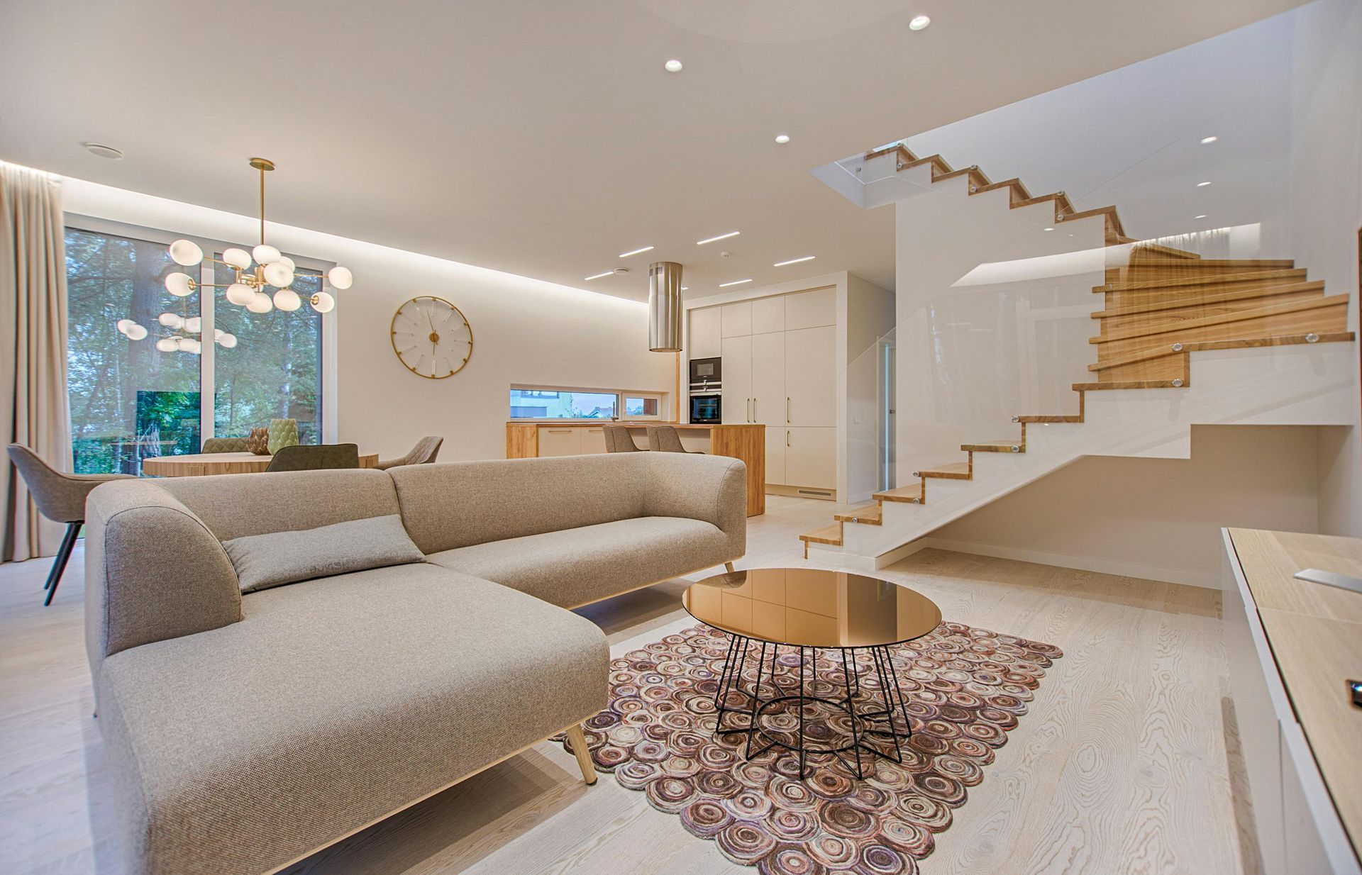 Open-concept living room with beige sectional sofa, wooden staircase, and gold accents.