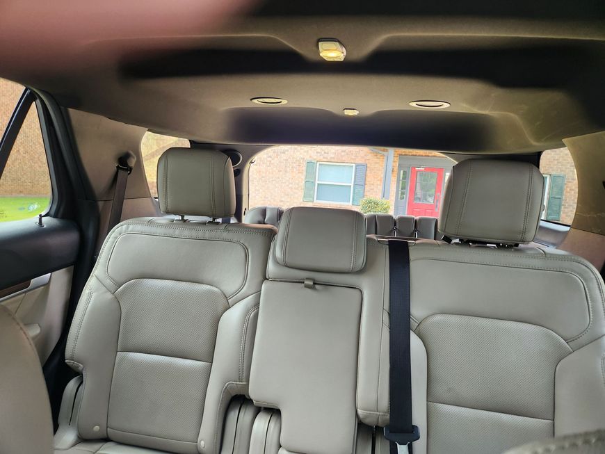 Car interior with three beige leather seats and seatbelts, viewed from the back toward the rear window.