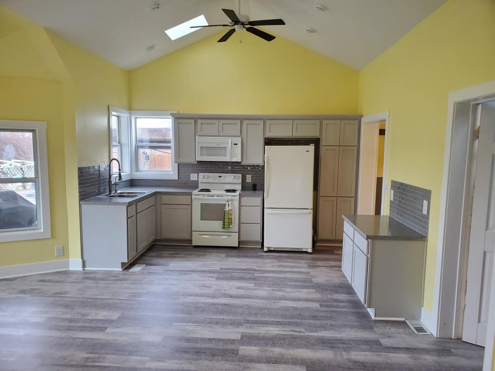 Empty kitchen with yellow walls, white appliances, and gray wood-style flooring.