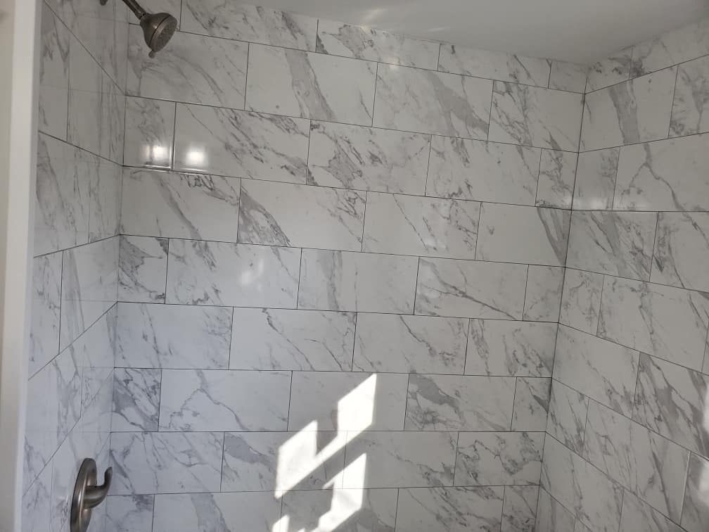 Marble-tiled shower corner with a chrome faucet and sunlight on the wall