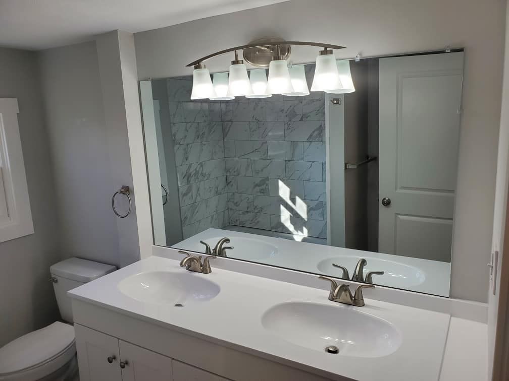 Bathroom vanity with double sinks, large mirror, and glass shower visible in the reflection