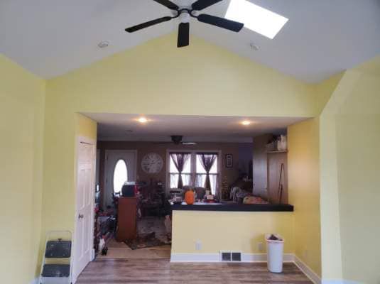 Living room opening to a kitchen with yellow walls, ceiling fan, and a black countertop bar.