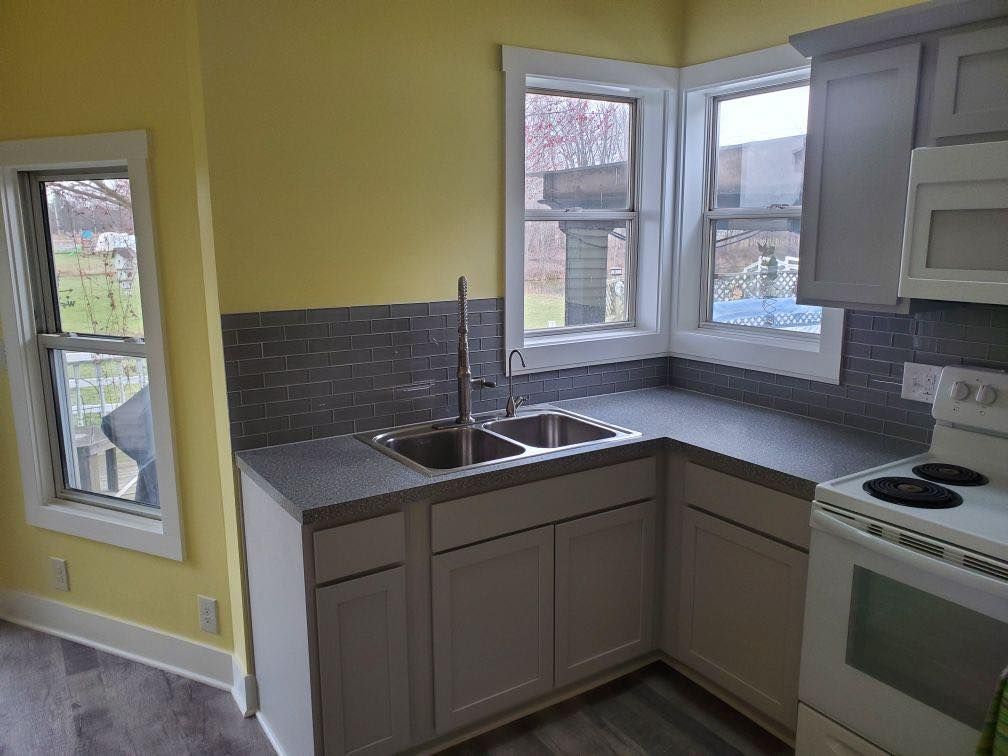 Modern kitchen with gray cabinets, yellow walls, stainless sink, and a stove by windows