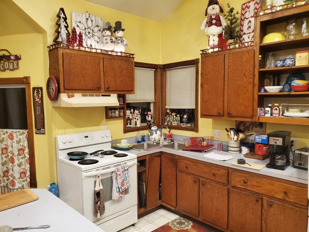Cozy yellow kitchen with white stove, wooden cabinets, sink, shelves, and patterned curtains
