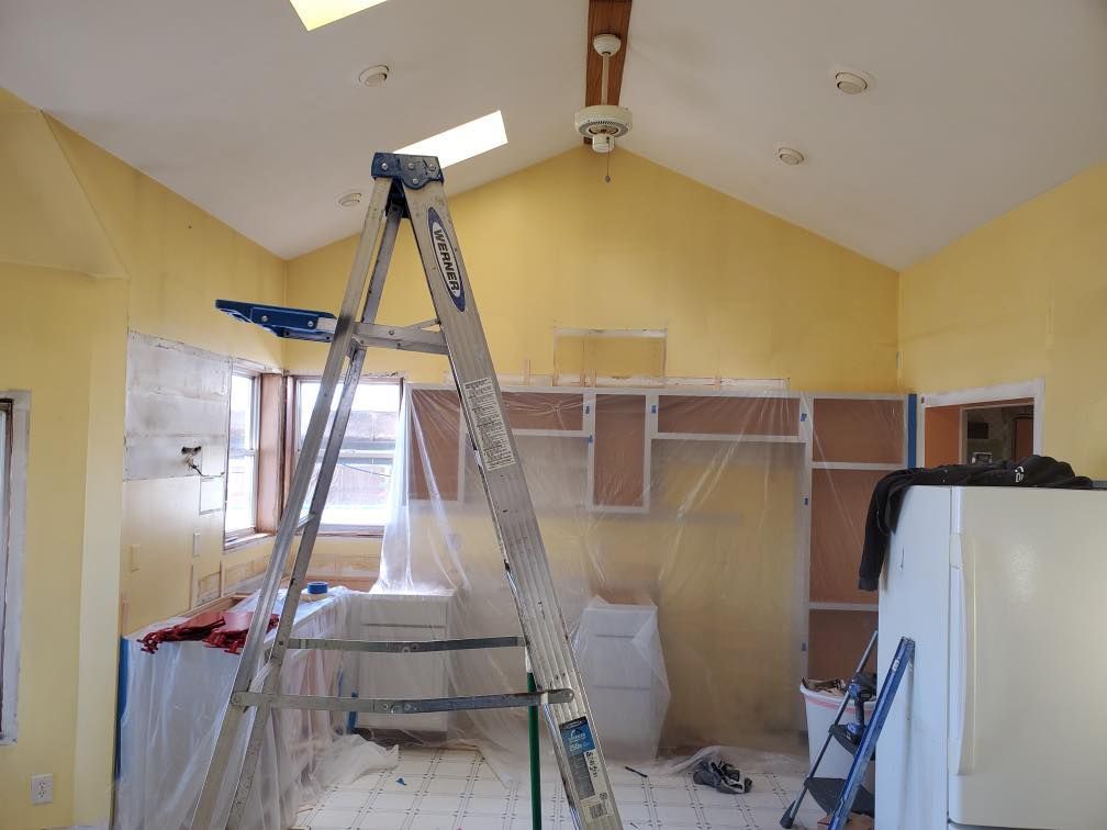 Renovation room with step ladders, scaffolding, and plastic-covered cabinets under a vaulted ceiling.
