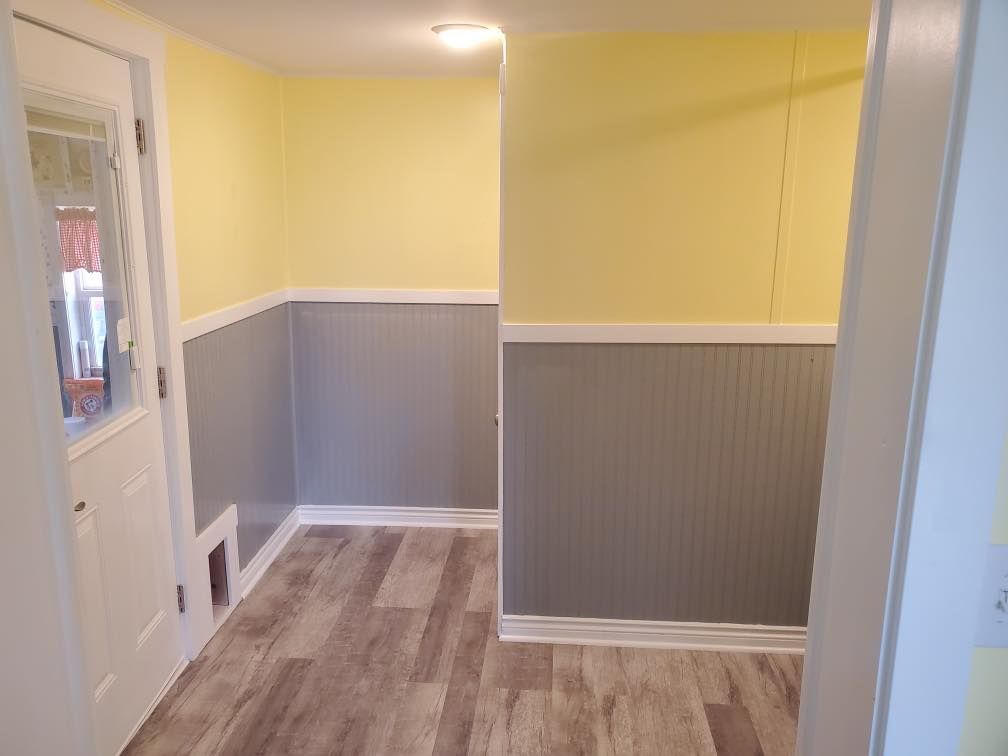 Empty room with yellow and gray walls, wood-look floor, white trim, and a door on the left.