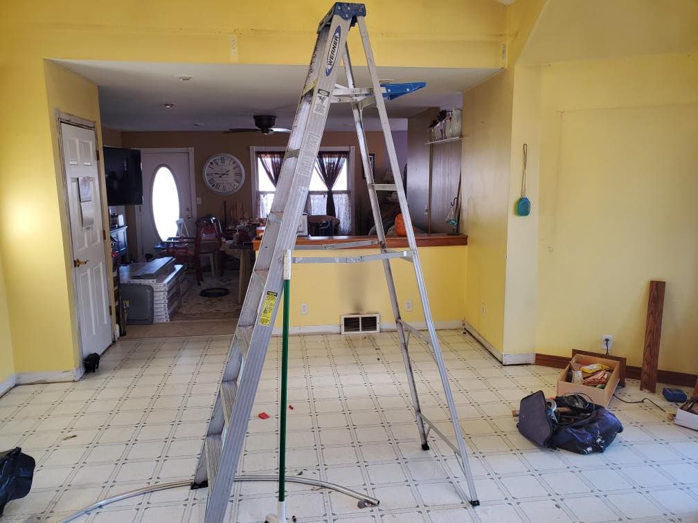Yellow room with a ladder under construction, tools and supplies scattered on the tile floor.
