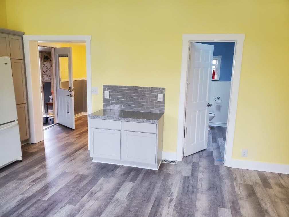 Empty kitchen with yellow walls, gray tile backsplash, white cabinets, and gray wood-look flooring