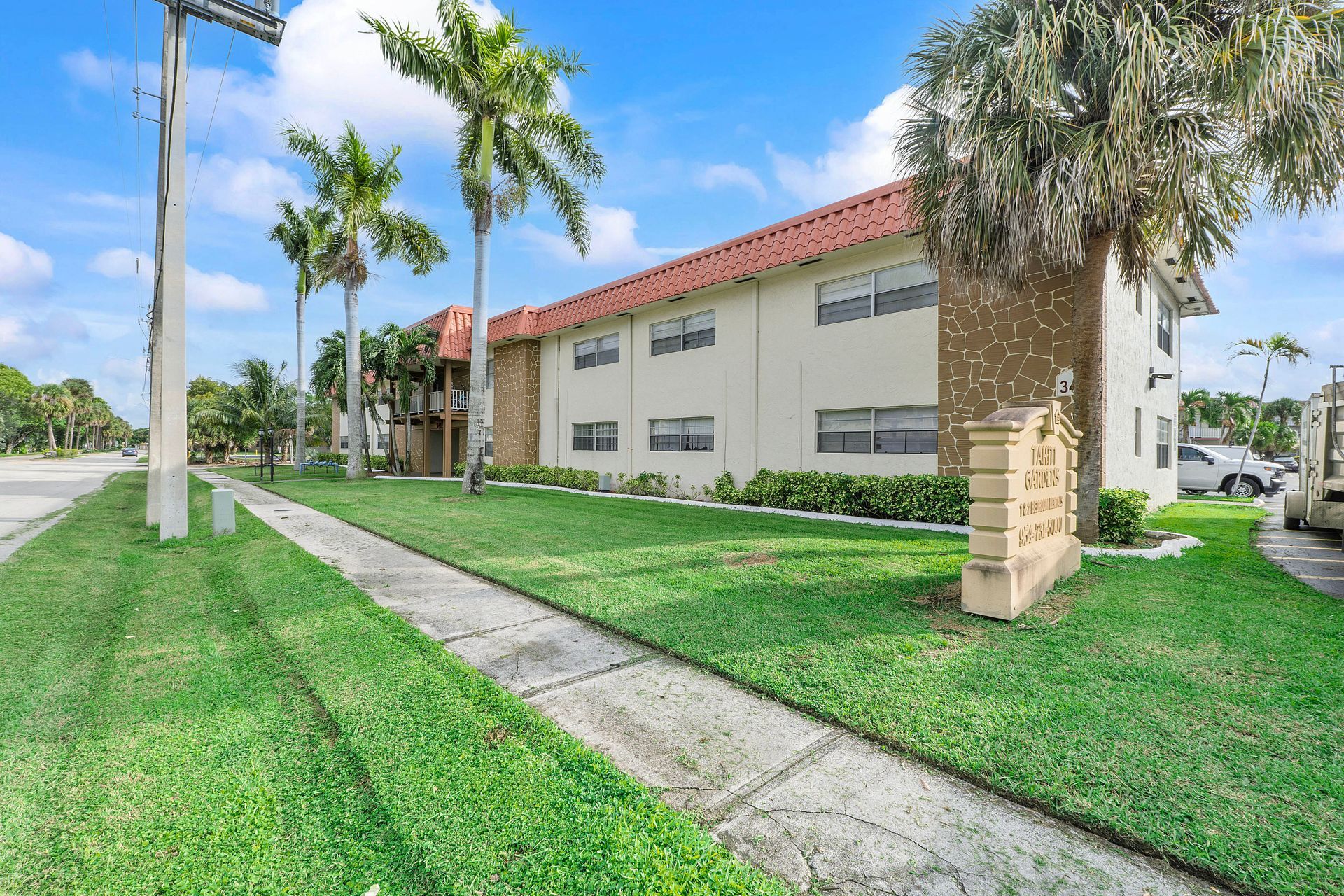 A white apartment building with a red roof and palm trees in front of it.