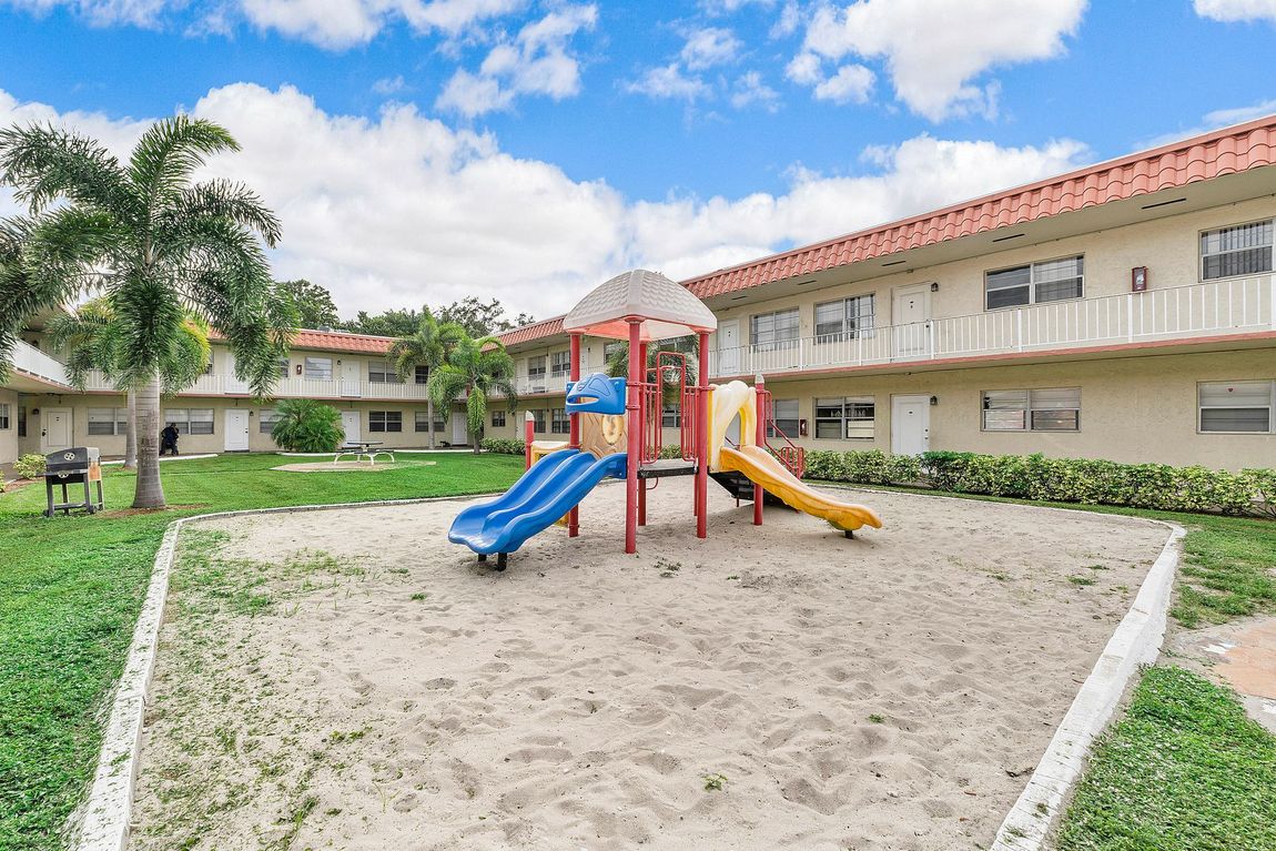 A playground with a slide and a sandbox in front of a building.