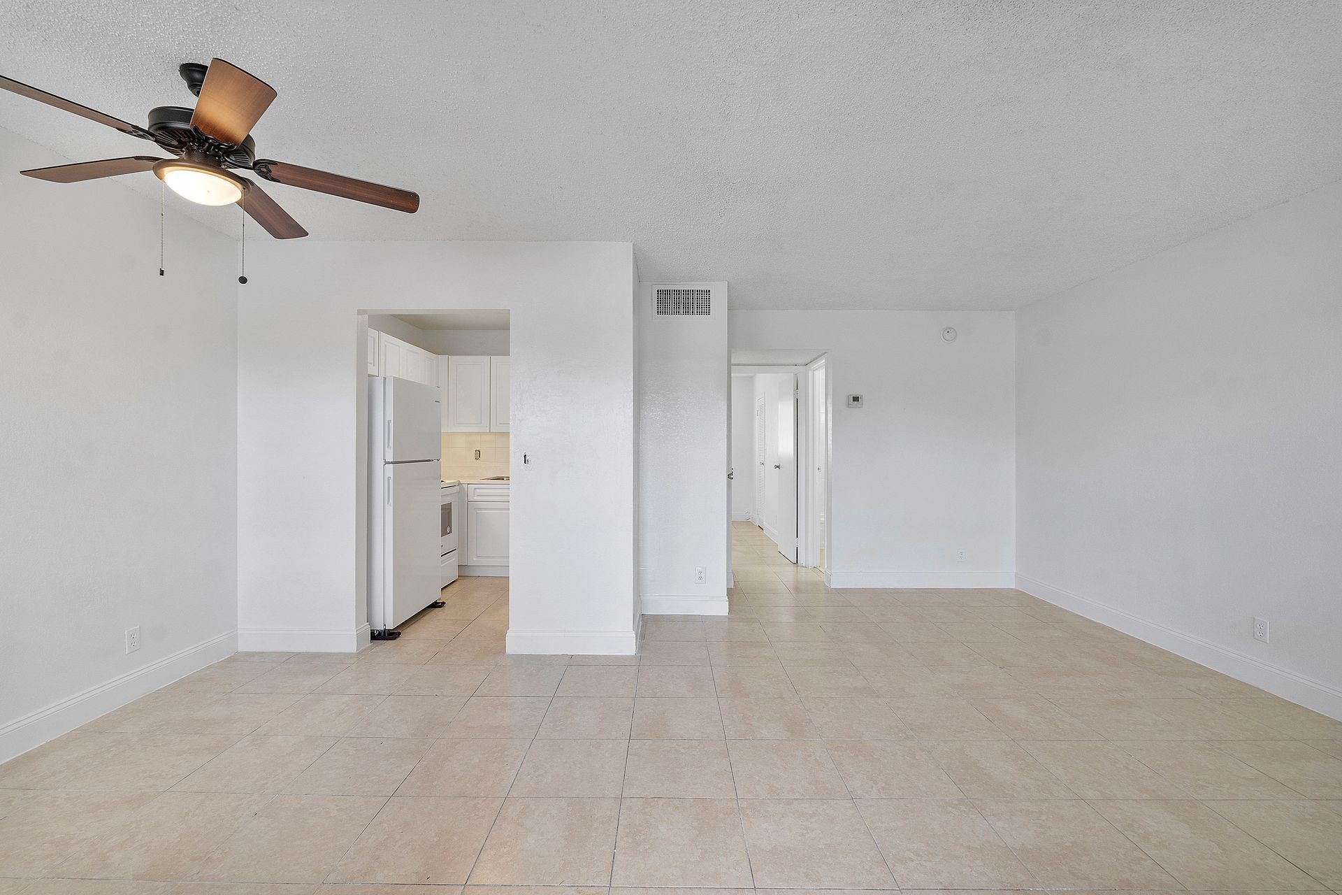 An empty living room with a ceiling fan and a refrigerator