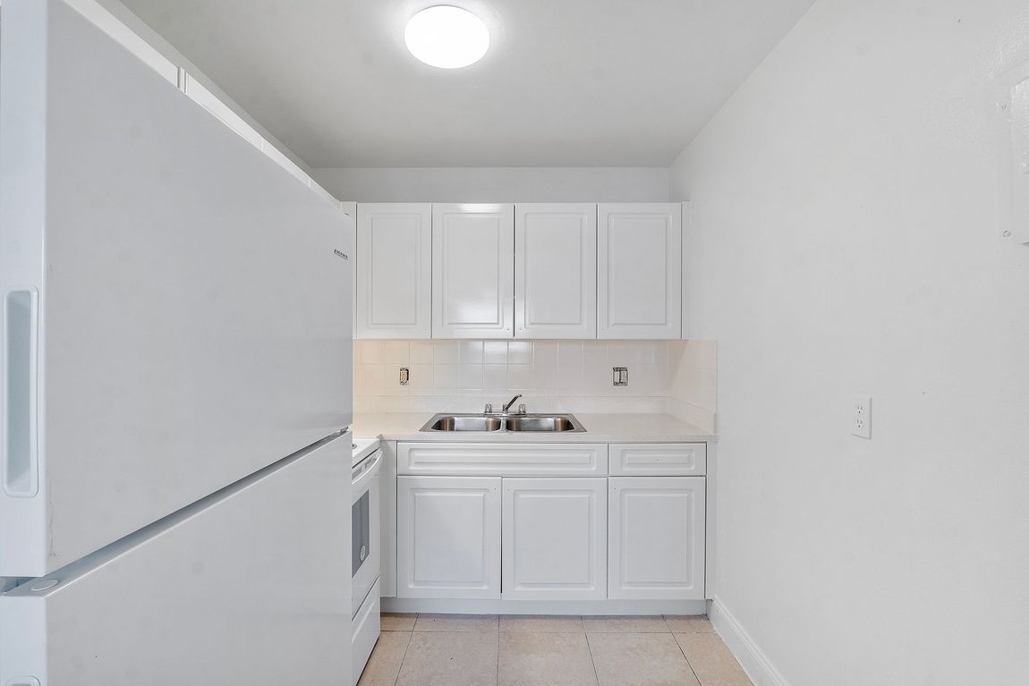 An empty kitchen with white cabinets and a white refrigerator