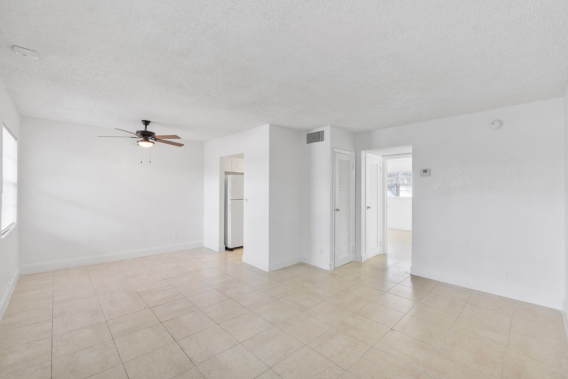 An empty living room with white walls and a ceiling fan.