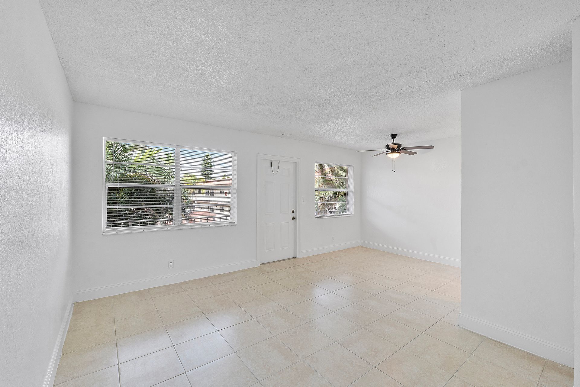 An empty living room with a ceiling fan and two windows.