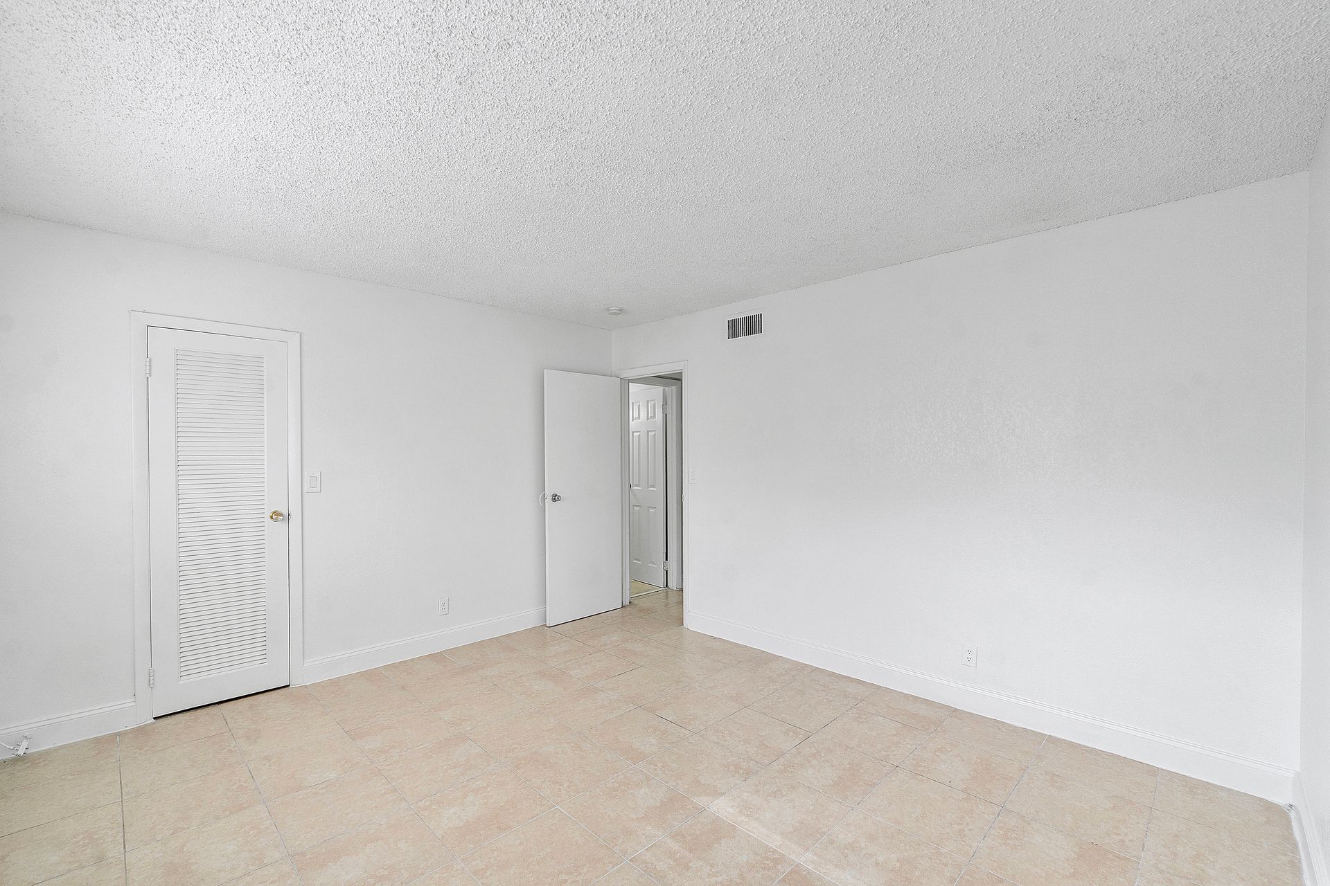 An empty living room with white walls and a tan carpet.