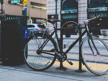 A bicycle is parked on the side of the road next to a trash can.