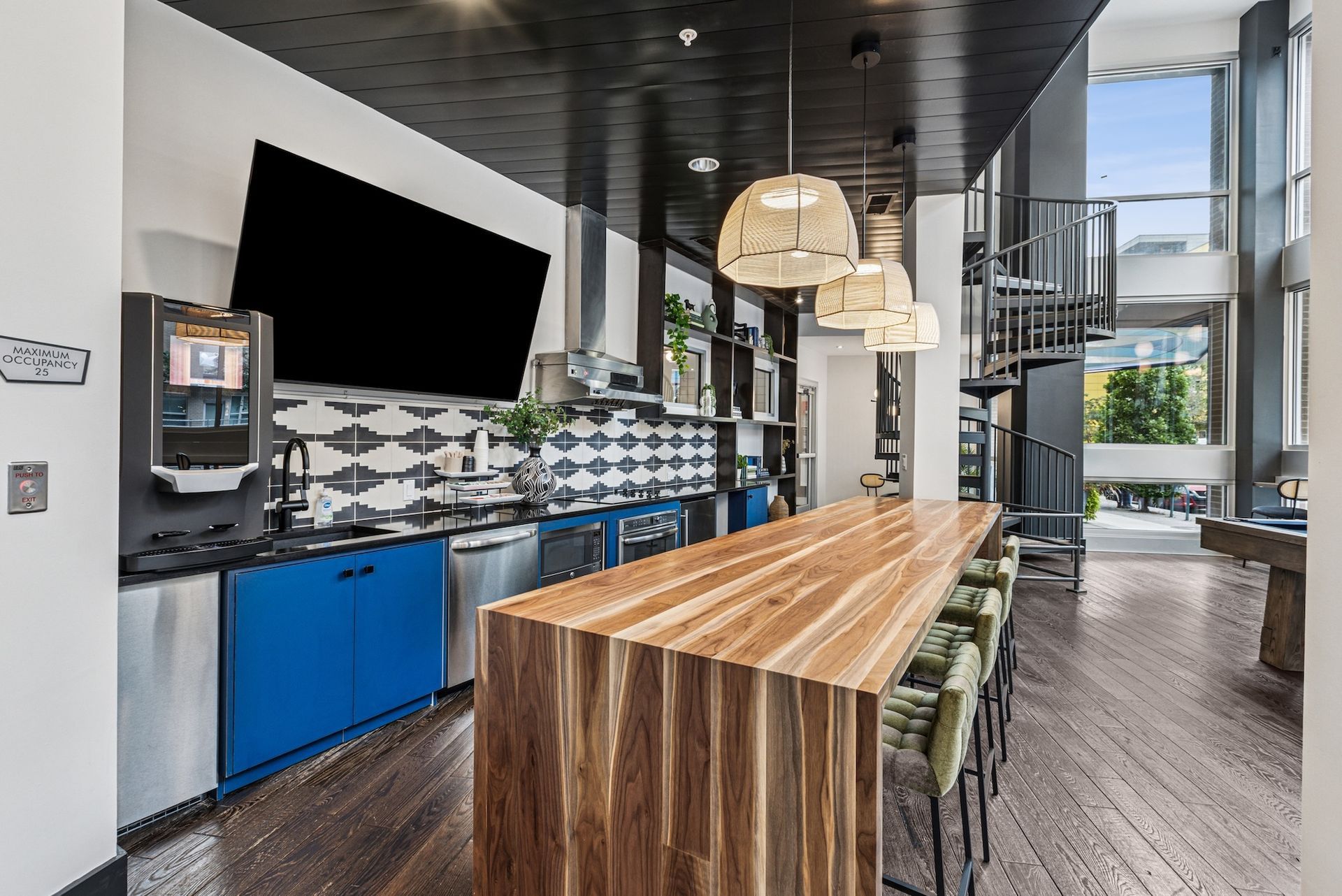 Modern kitchen with wooden island, blue cabinets, spiral staircase, and large TV.