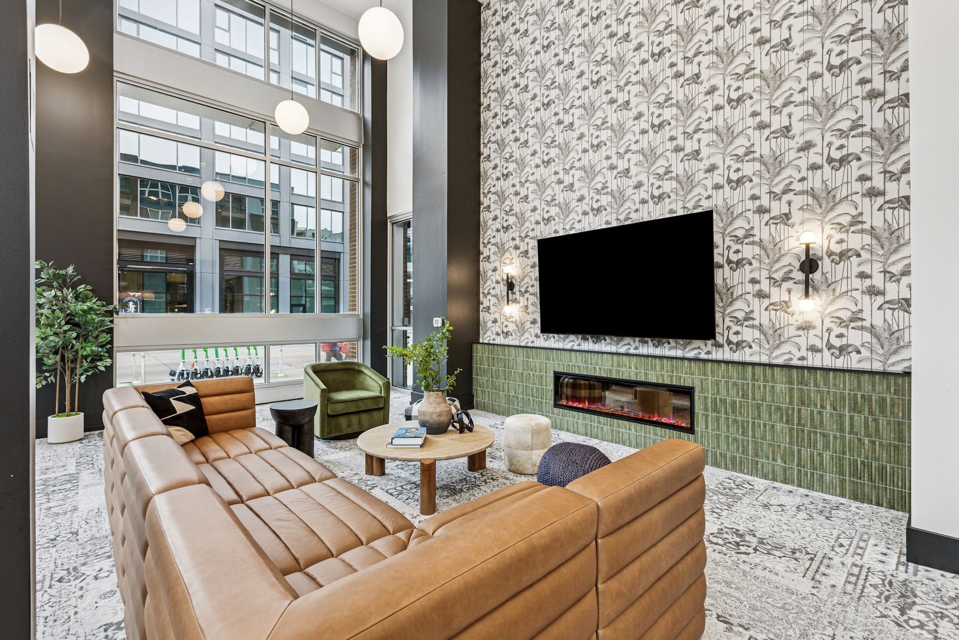 Modern living room with tan sectional sofa, TV over a fireplace, patterned wallpaper, and large windows.