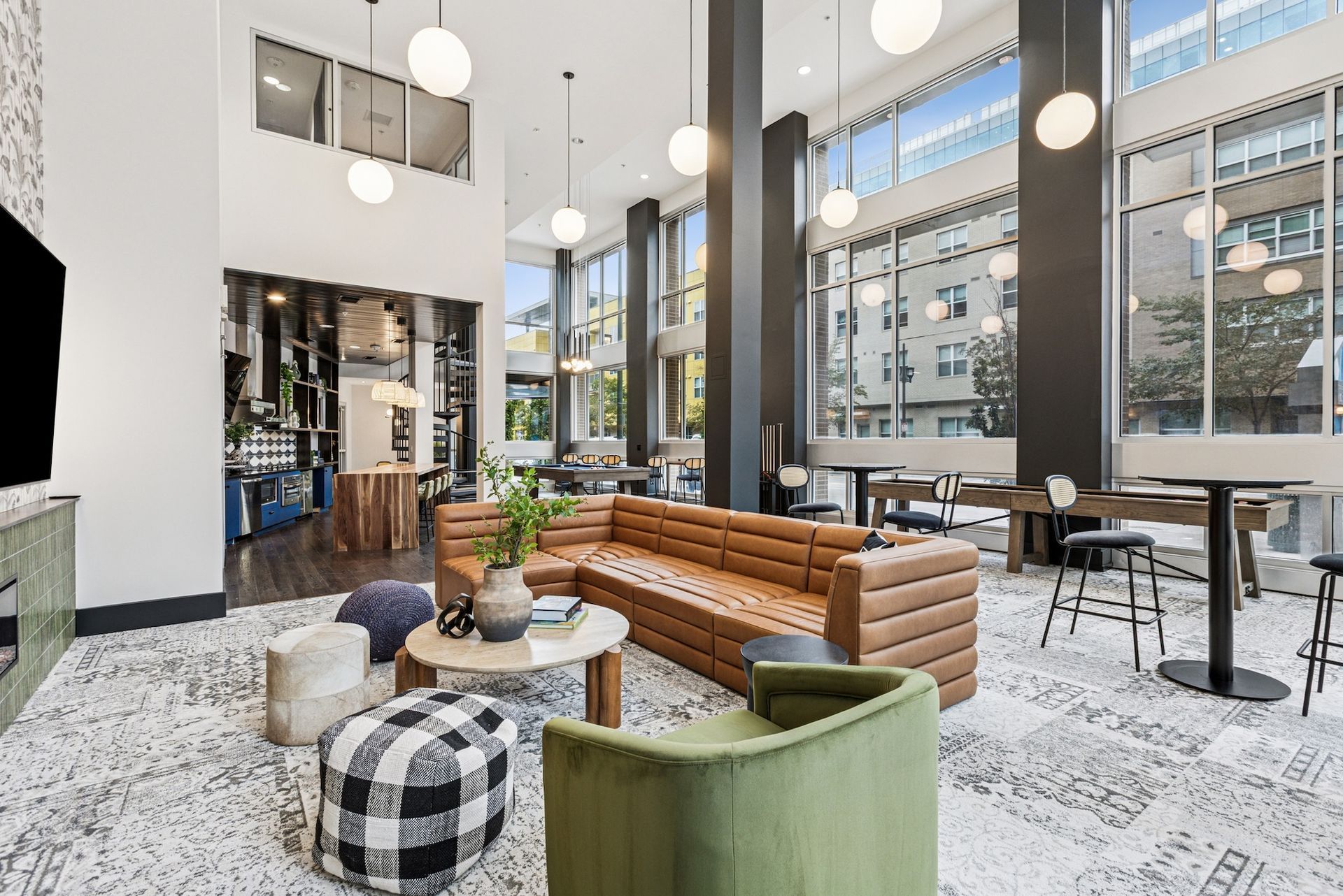 Lounge area with a brown leather sofa, high windows, and round pendant lights. Tables and seating are available.