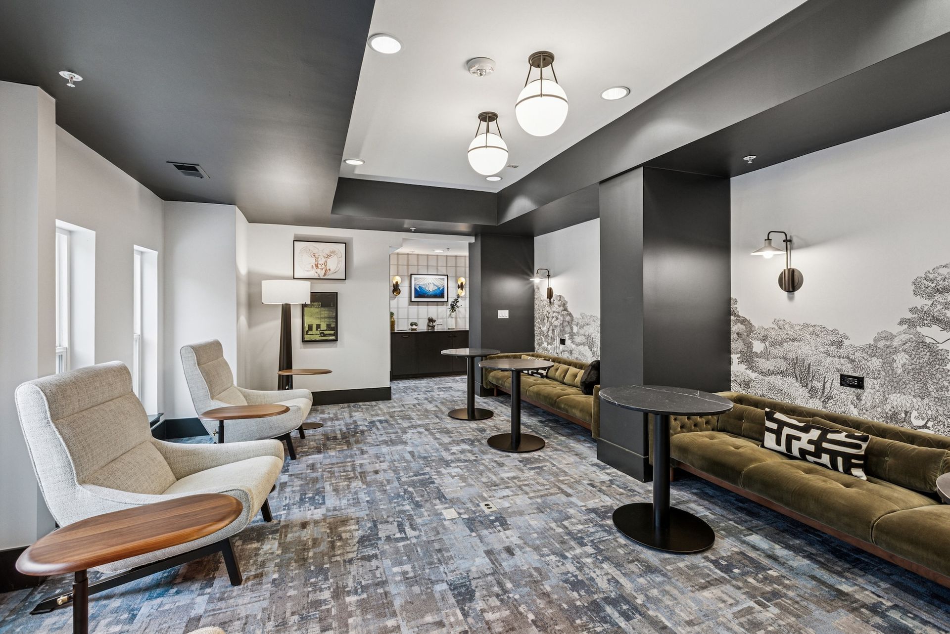 Modern lounge area with seating, artwork, and small tables; dark gray ceiling and accent walls.
