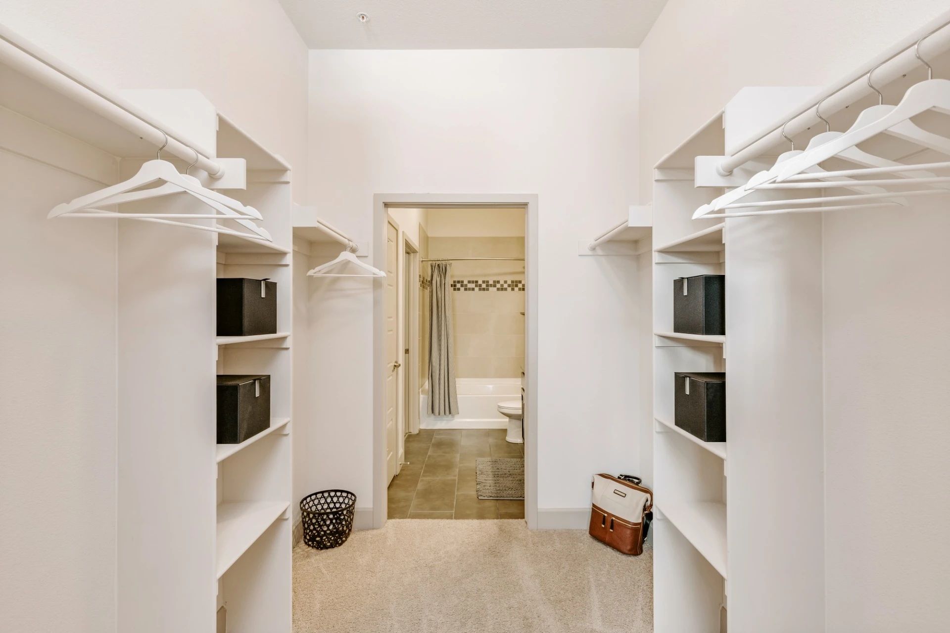 A walk in closet with a bathroom in the background.