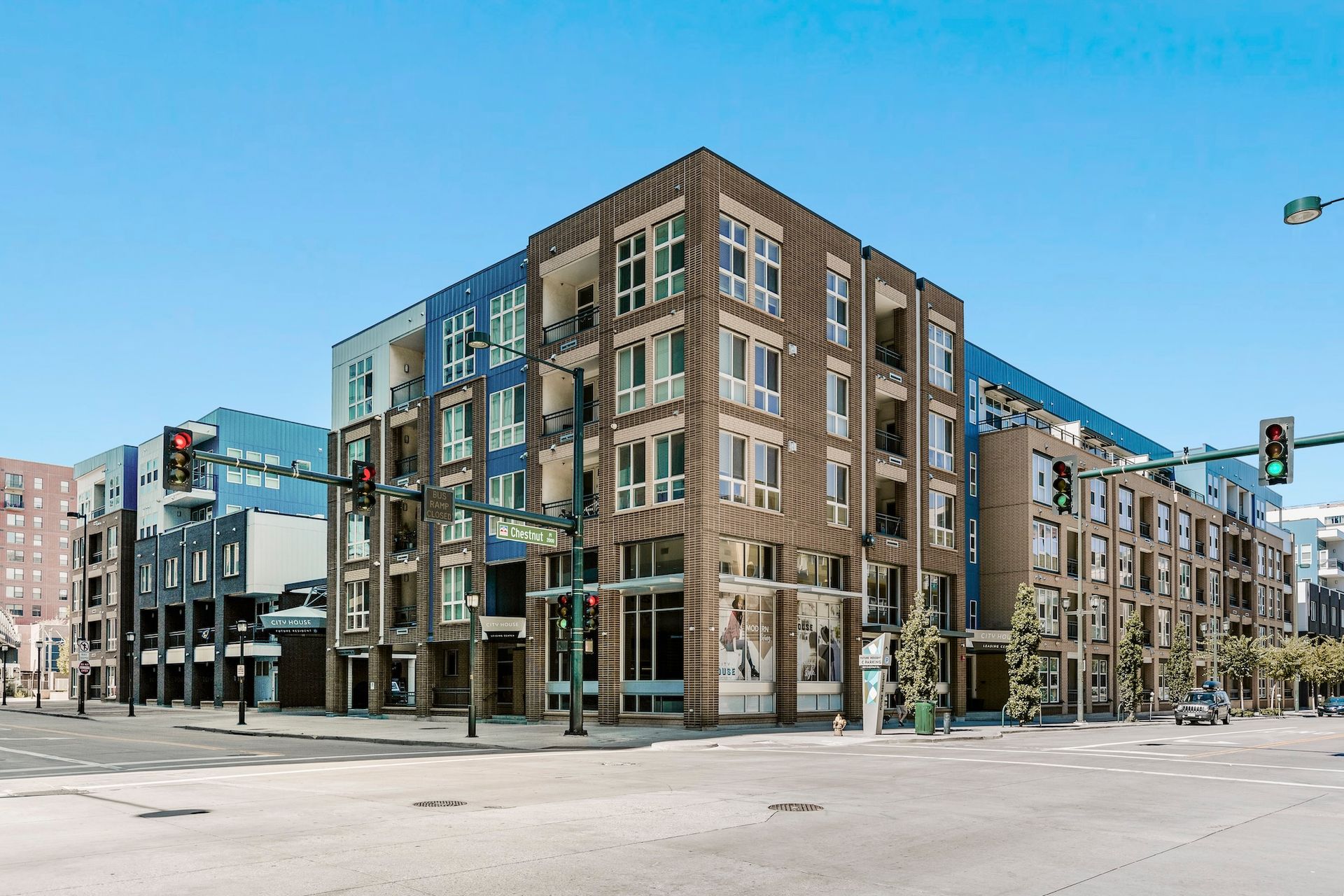 Modern multi-story building on a city street corner; blue, brown, and glass facade, sunny day.