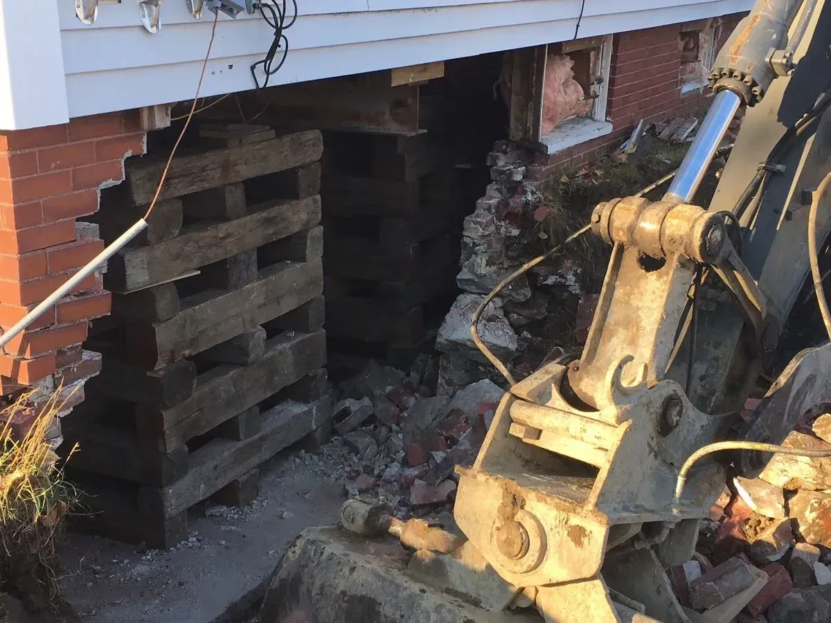 An excavator is demolishing a brick wall of a house.
