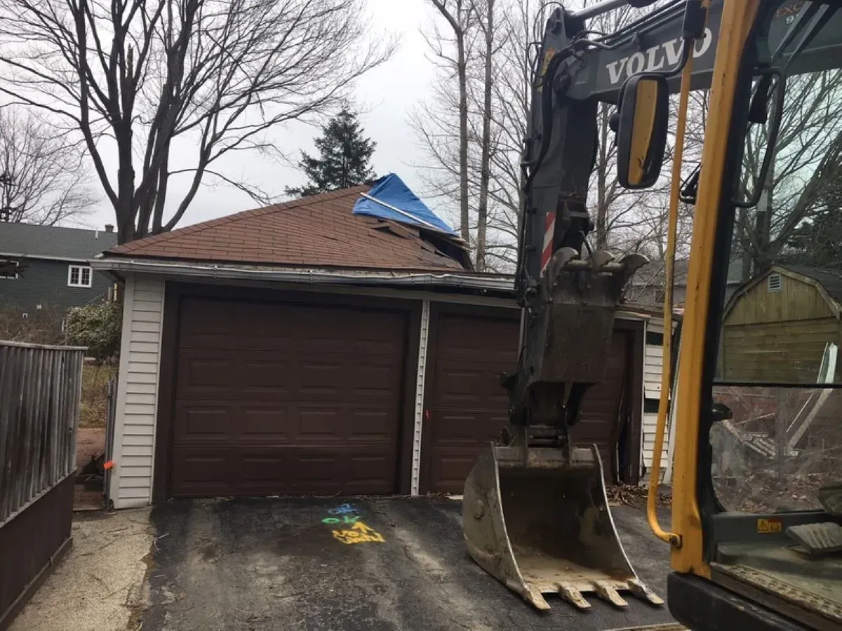 A volvo excavator is digging in front of a garage.