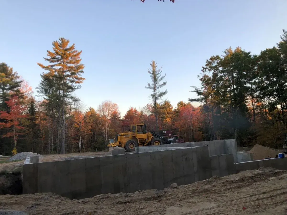 A yellow bulldozer is working on a concrete wall in the middle of a forest.