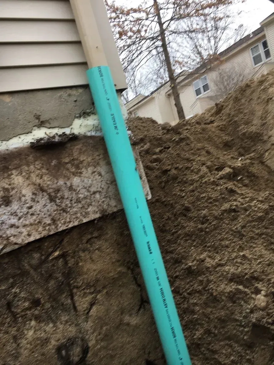 A green pipe is sitting on top of a pile of dirt next to a house.