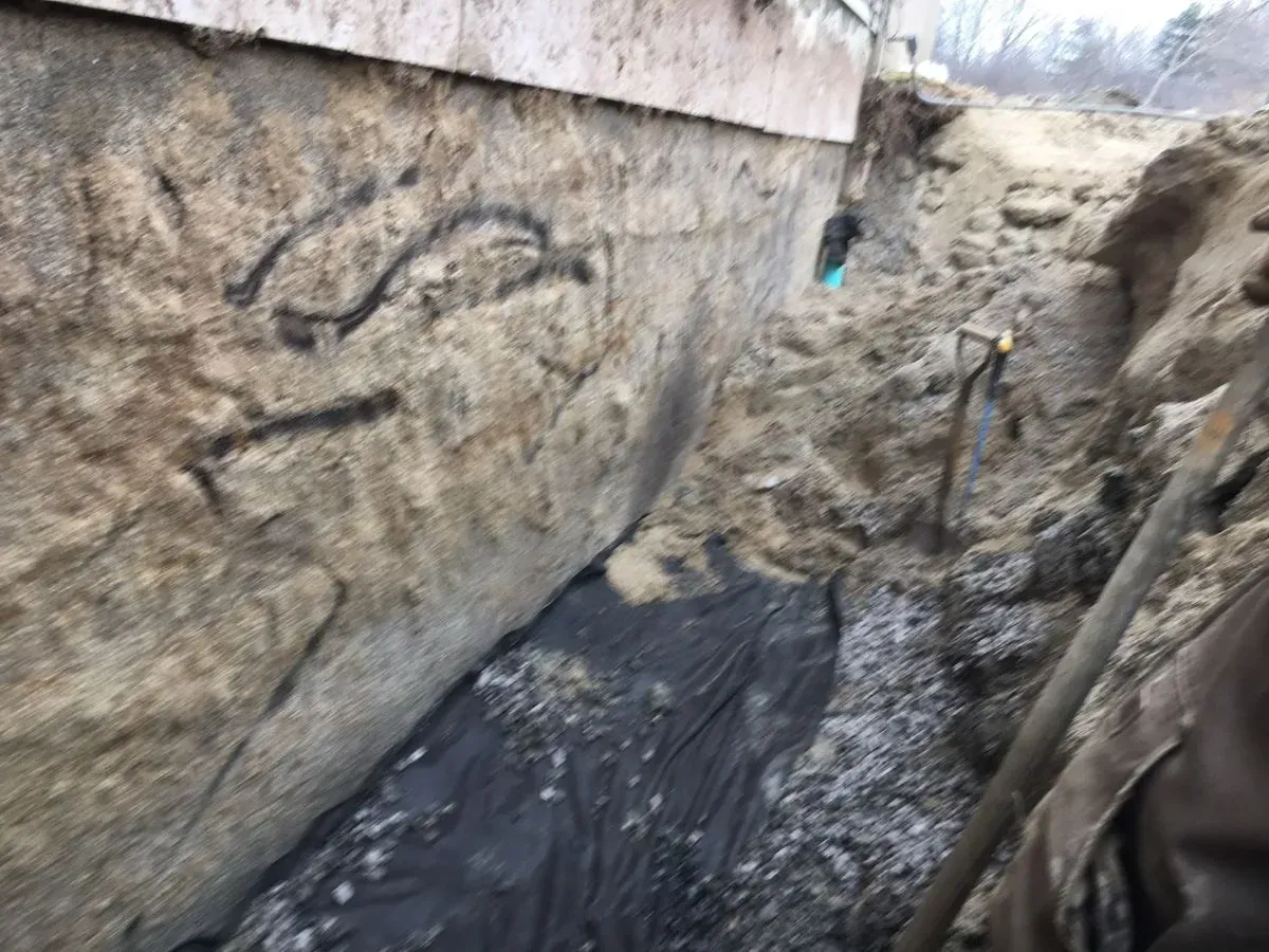 A person is digging a hole in the ground next to a wall.