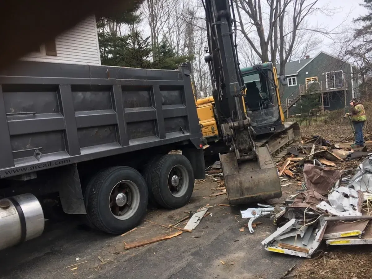 A dump truck is driving down a road next to an excavator.