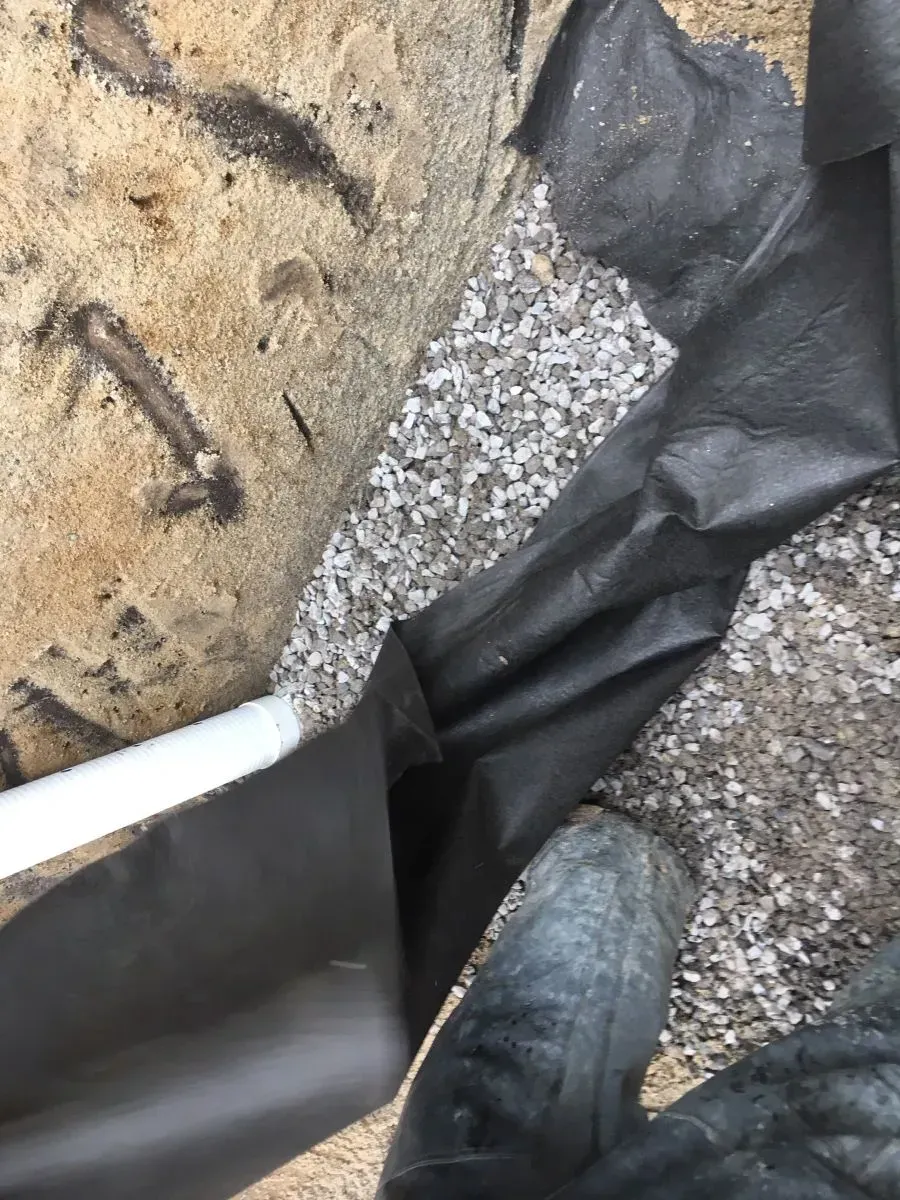 A person is holding a piece of black plastic covering a rock.