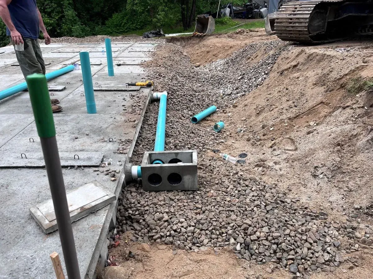A man is standing next to a pile of gravel and pipes.