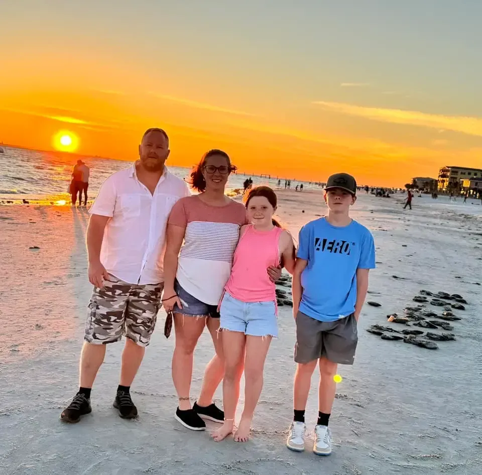 A group of people posing for a picture on a beach at sunset