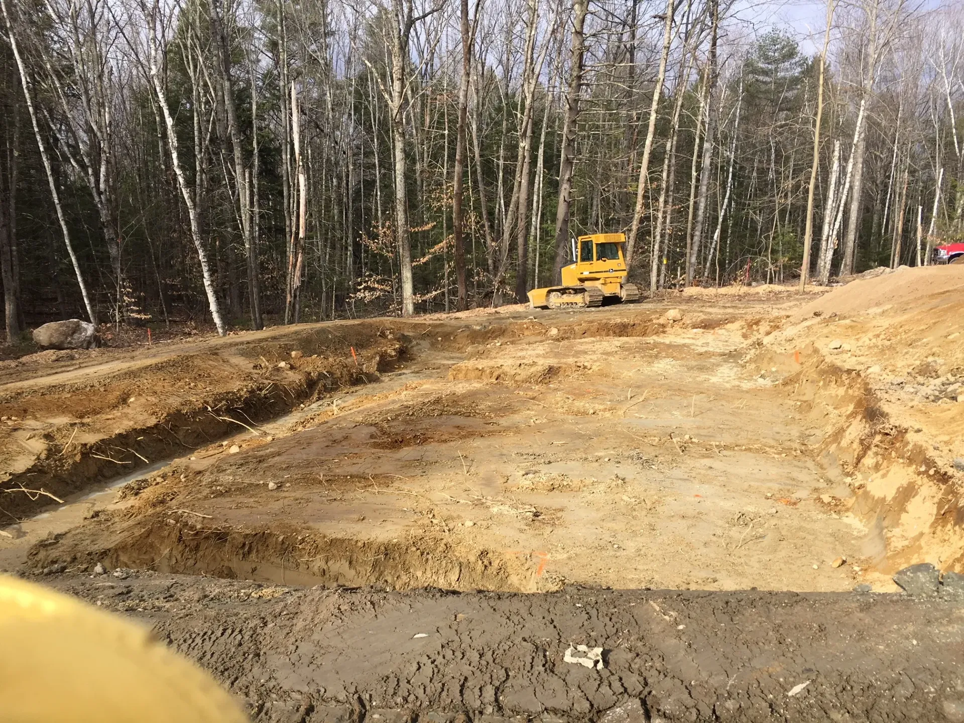 A yellow bulldozer is digging a hole in the dirt in the middle of a forest.