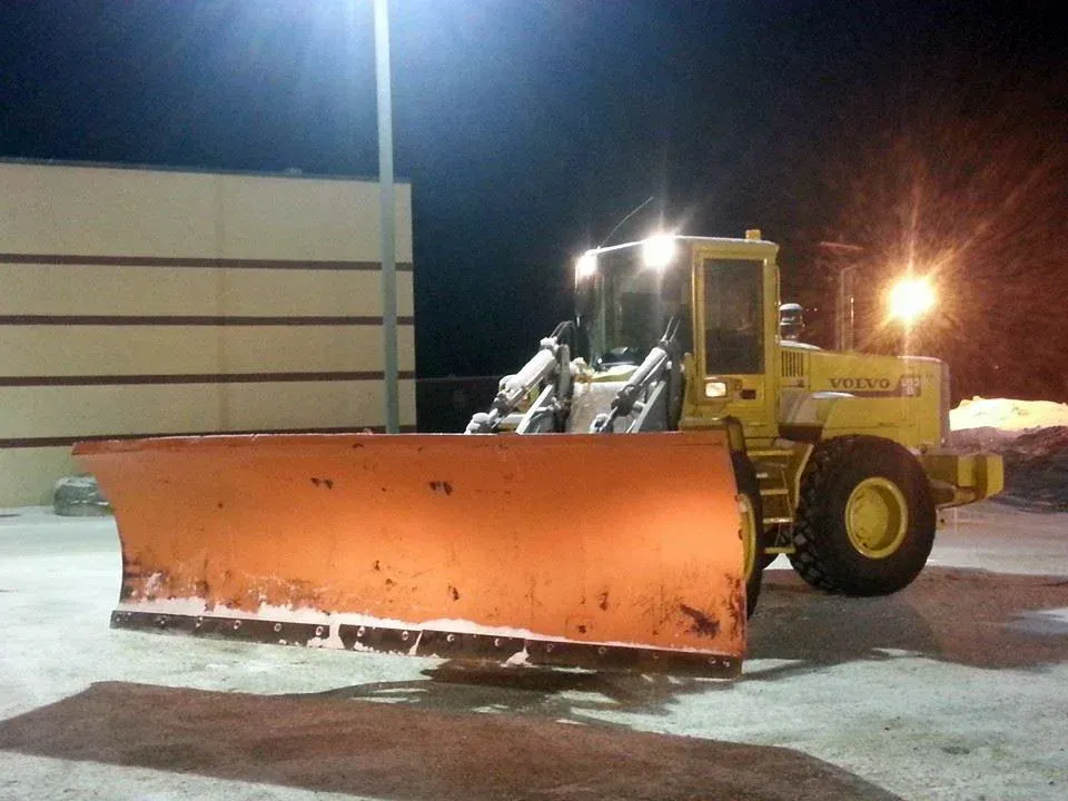 A yellow snow plow is parked in front of a building at night