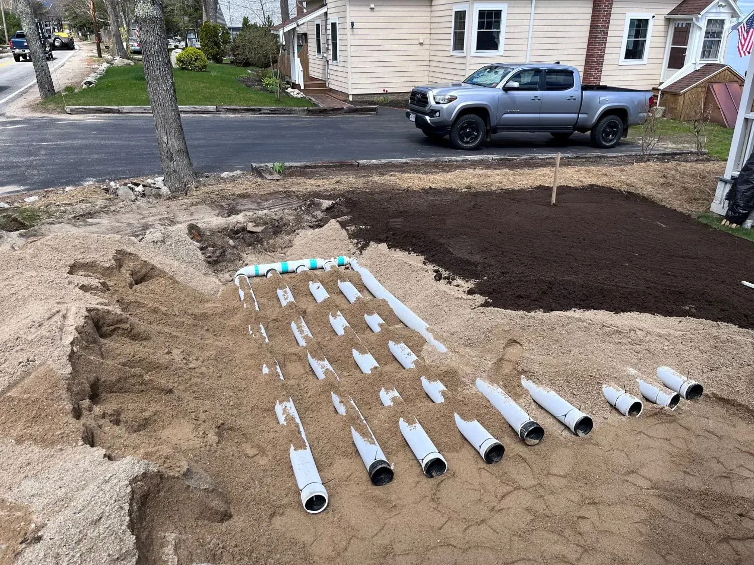 A truck is parked next to a pile of pipes in the dirt.