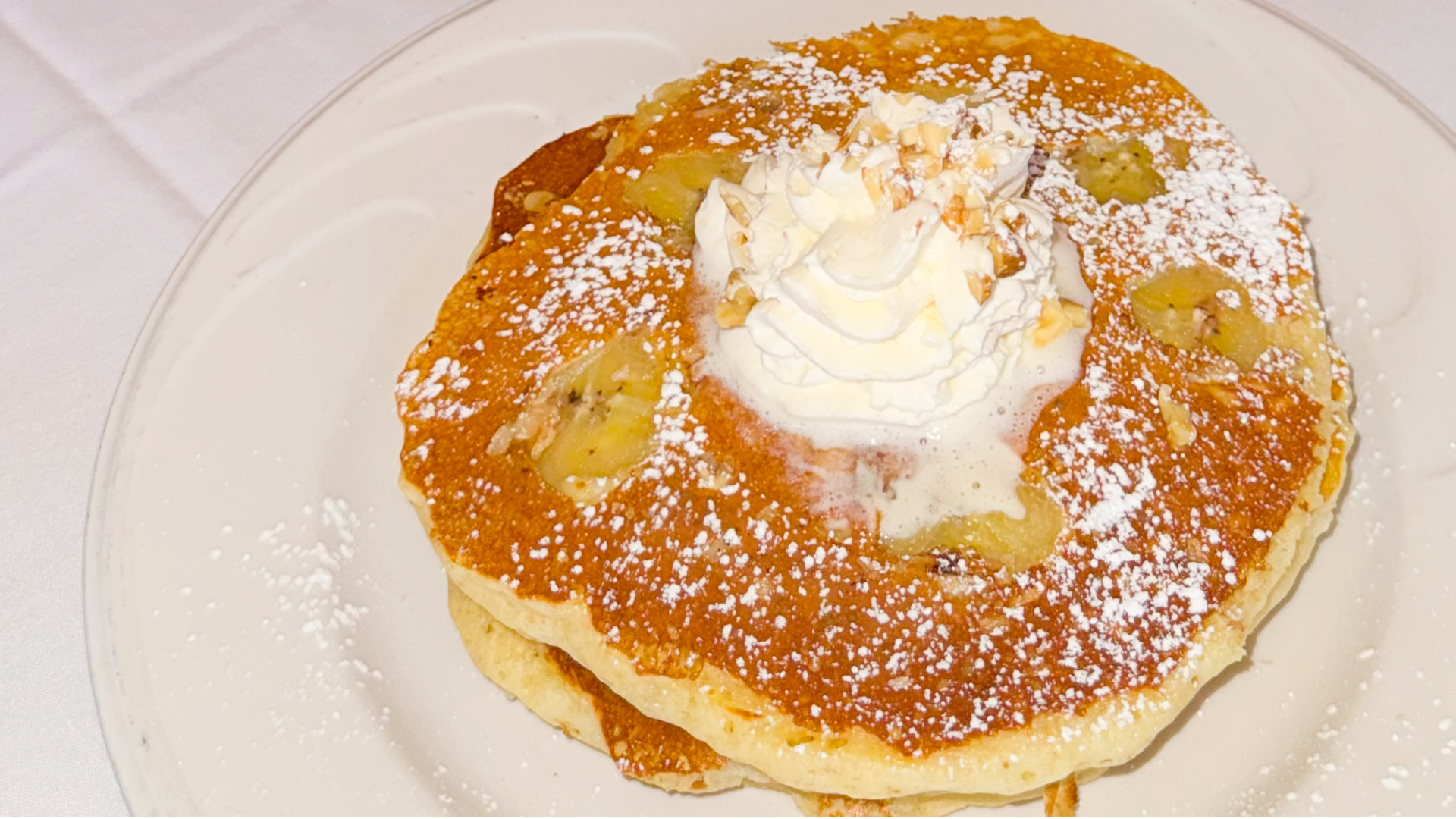 Golden pancakes layered with banana and walnut, dusted with powdered sugar and finished with a dollop of whipped cream.