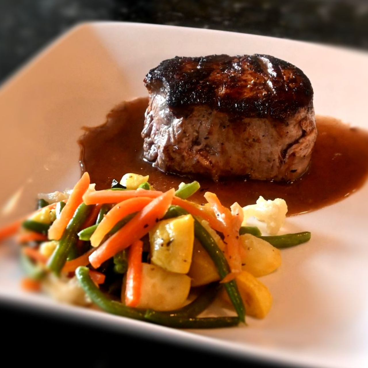 Perfectly seared filet mignon topped with a rich sauce, plated with vegetables for a refined fine-dining presentation.