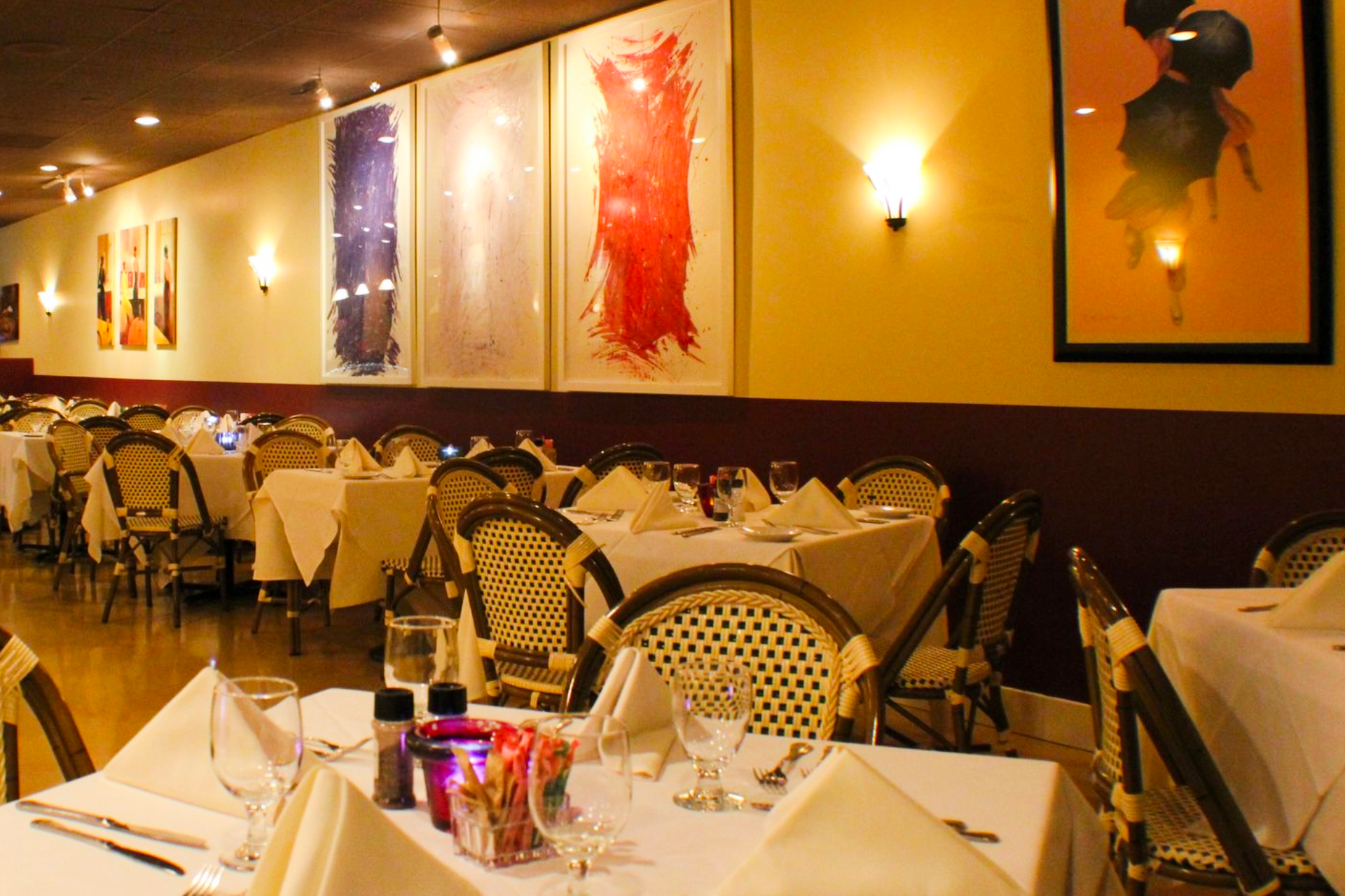 Warm, elegant dining room at Chez Pierre Bistro featuring white tablecloths, French bistro chairs, soft ambient lighting, and colorful modern art on the walls, capturing the intimate, classic French atmosphere of the restaurant.