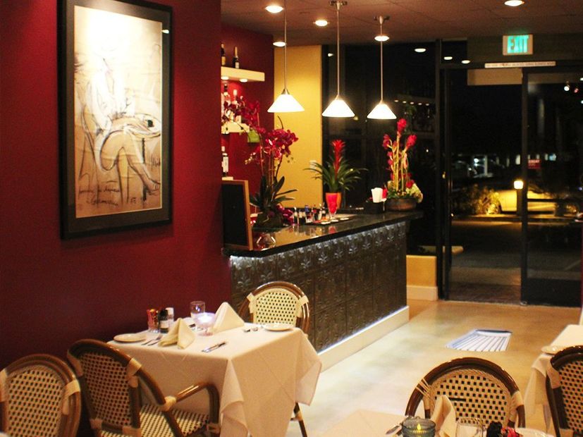 Intimate bar area inside Chez Pierre Bistro featuring soft pendant lighting, elegant floral arrangements, French bistro chairs, and warm red and gold tones that create a cozy, sophisticated dining ambiance.