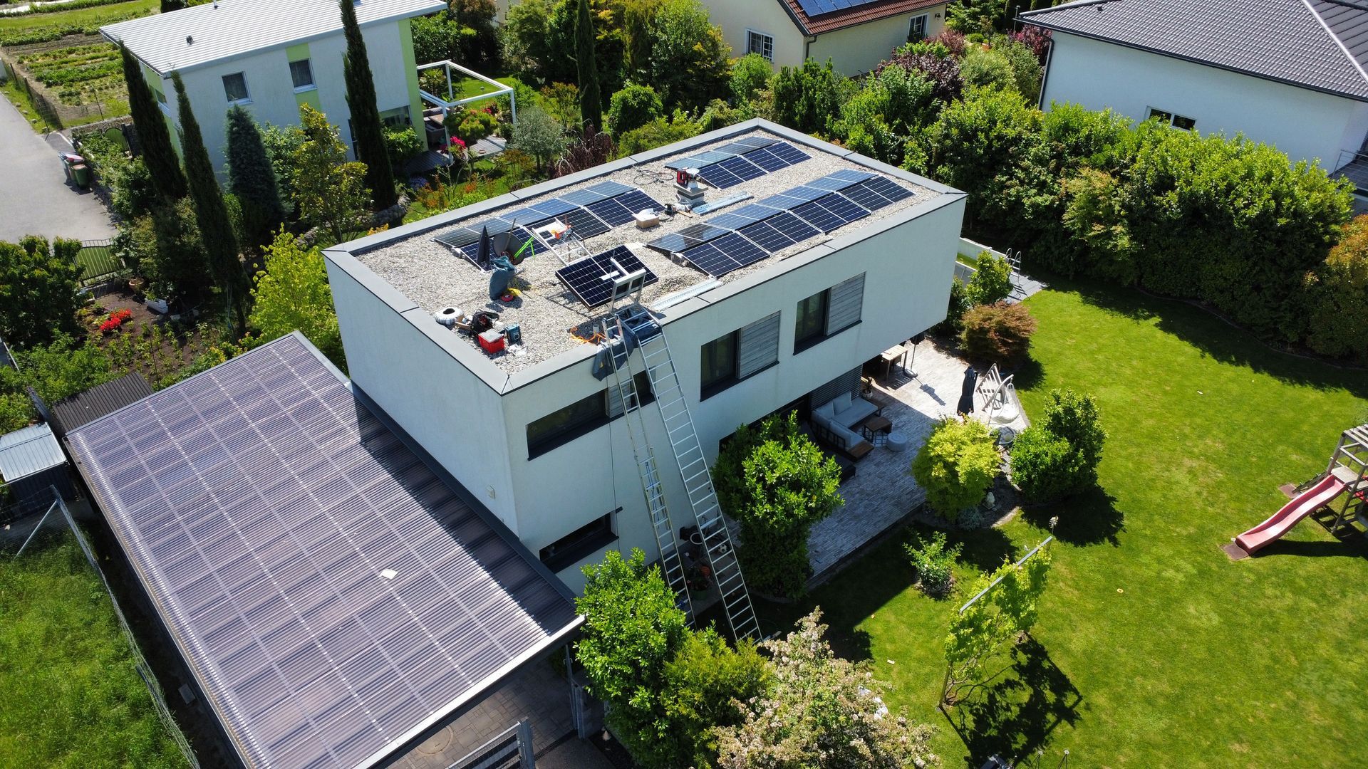 Luftaufnahme eines modernen weißen Hauses mit Solaranlage, Carport und grünem Garten
