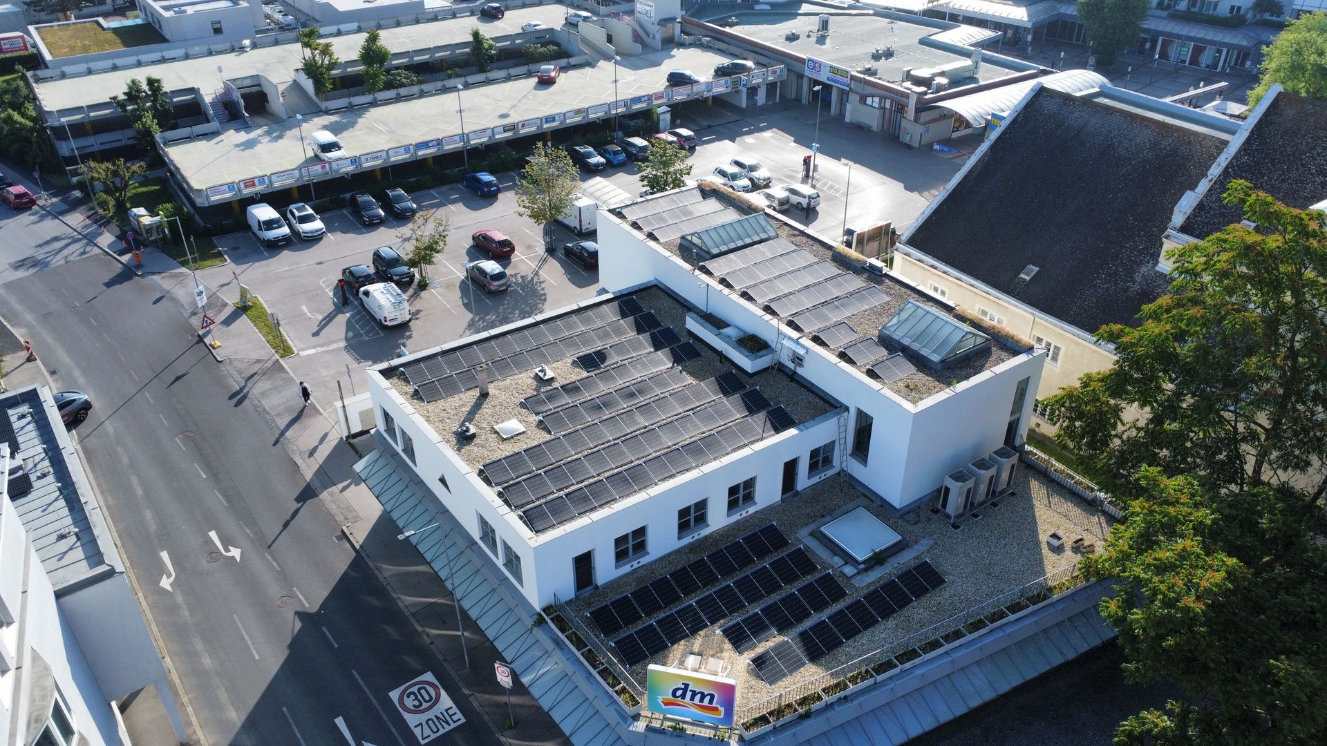 Luftaufnahme eines weißen Gebäudes mit Flachdach neben einer Straße und einem Parkplatz in einem Industriegebiet