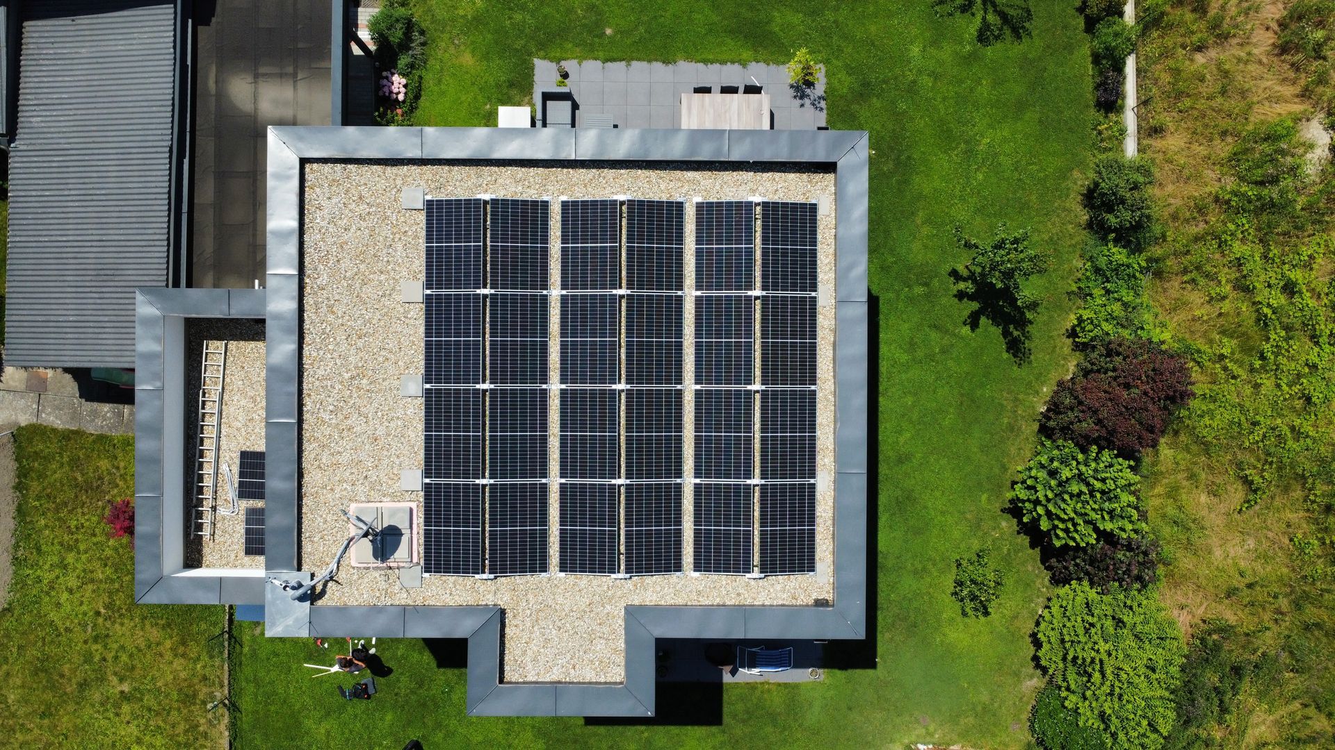 Luftaufnahme eines Hausdachs mit Solarpaneelen, umgeben von grünen Bäumen und Rasen