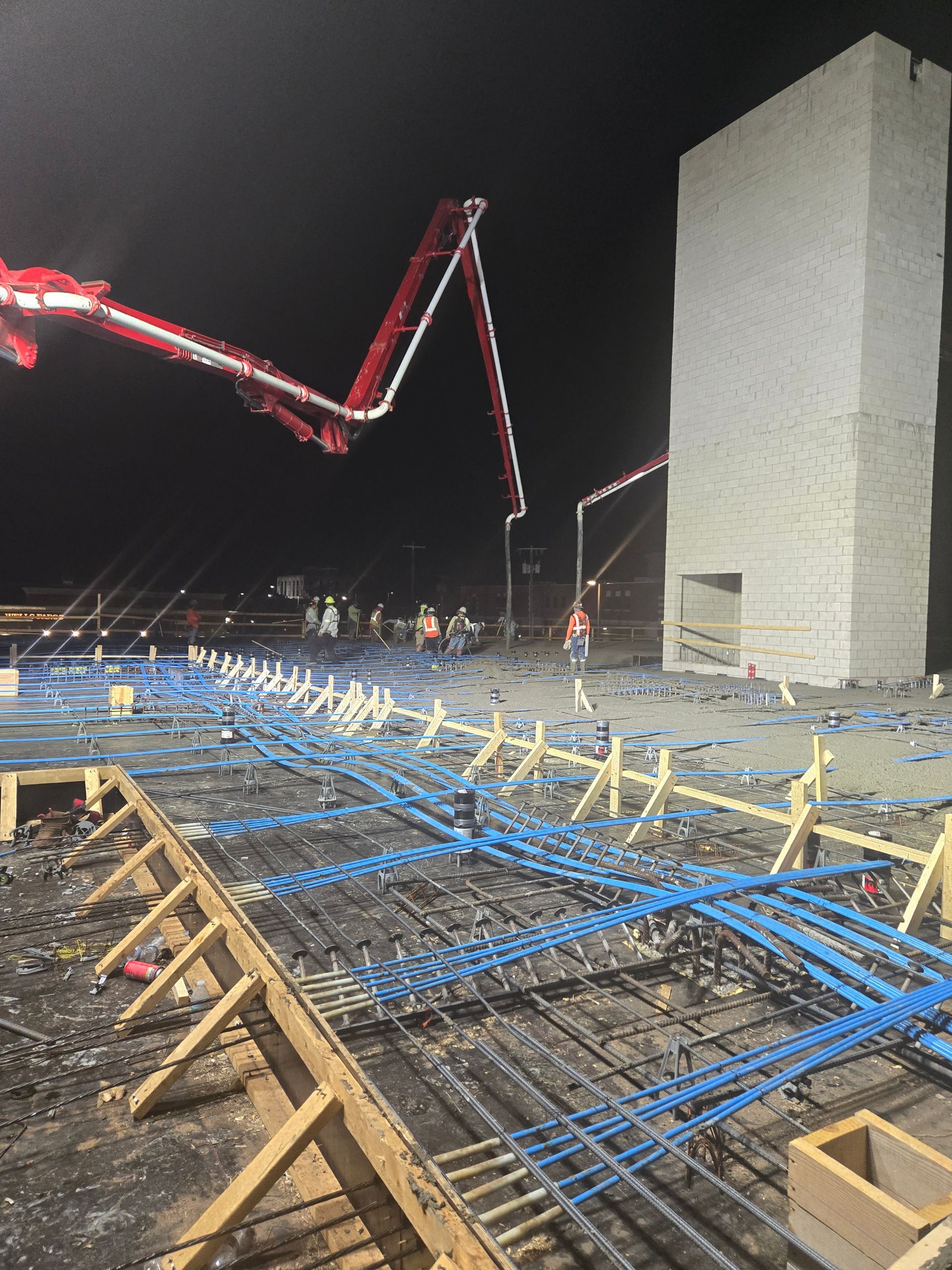 A concrete pump is being used to pour concrete on a construction site at night.