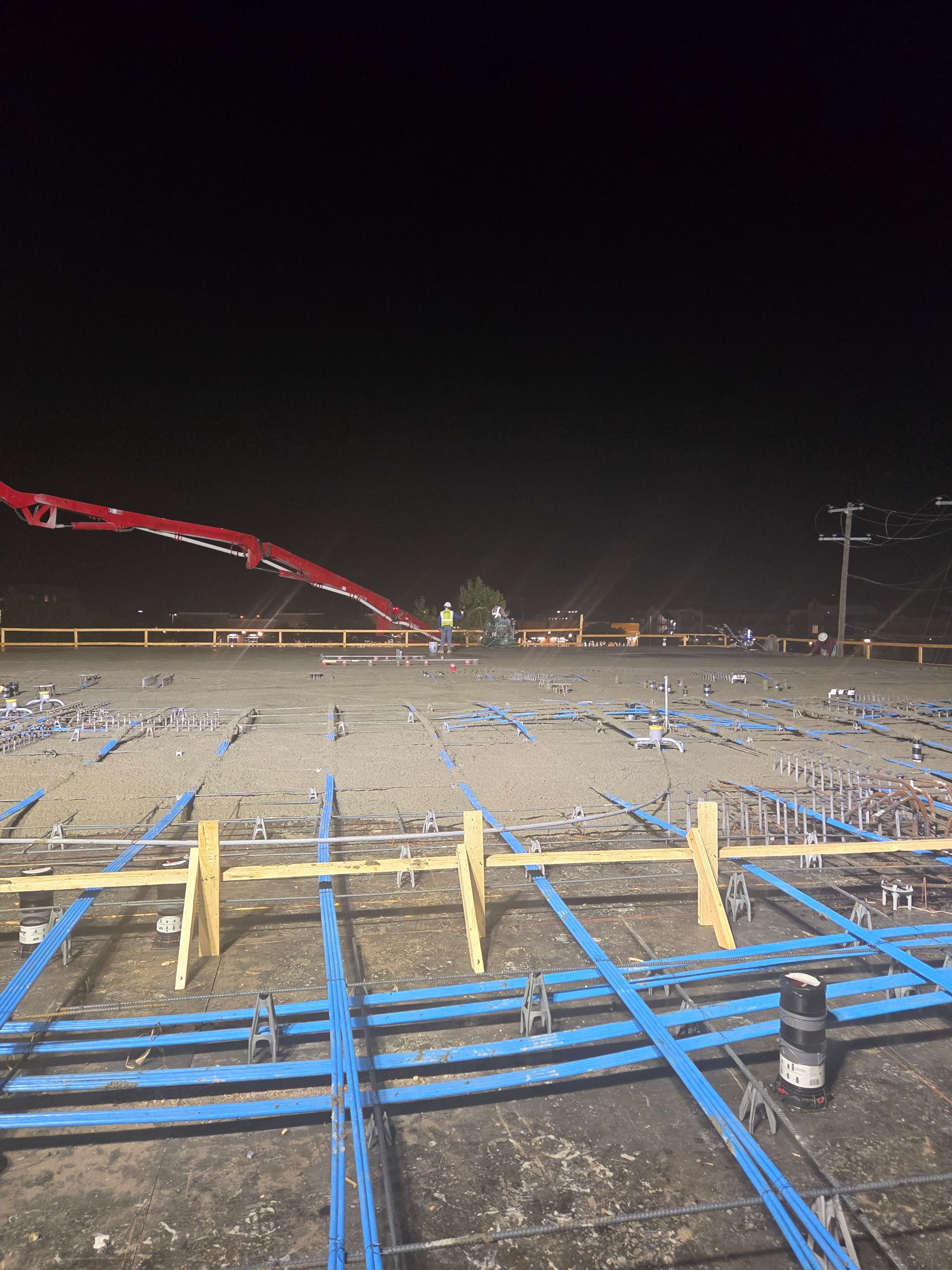 A construction site at night with a concrete pump in the background.