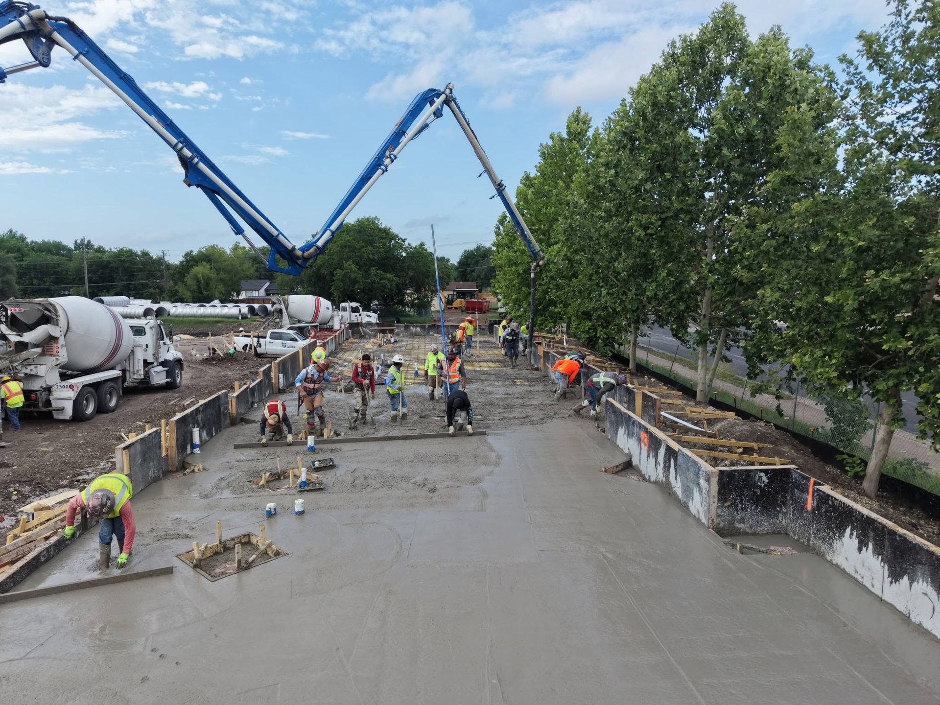 Construction workers pouring concrete in a large roadway project with cement trucks and pumps