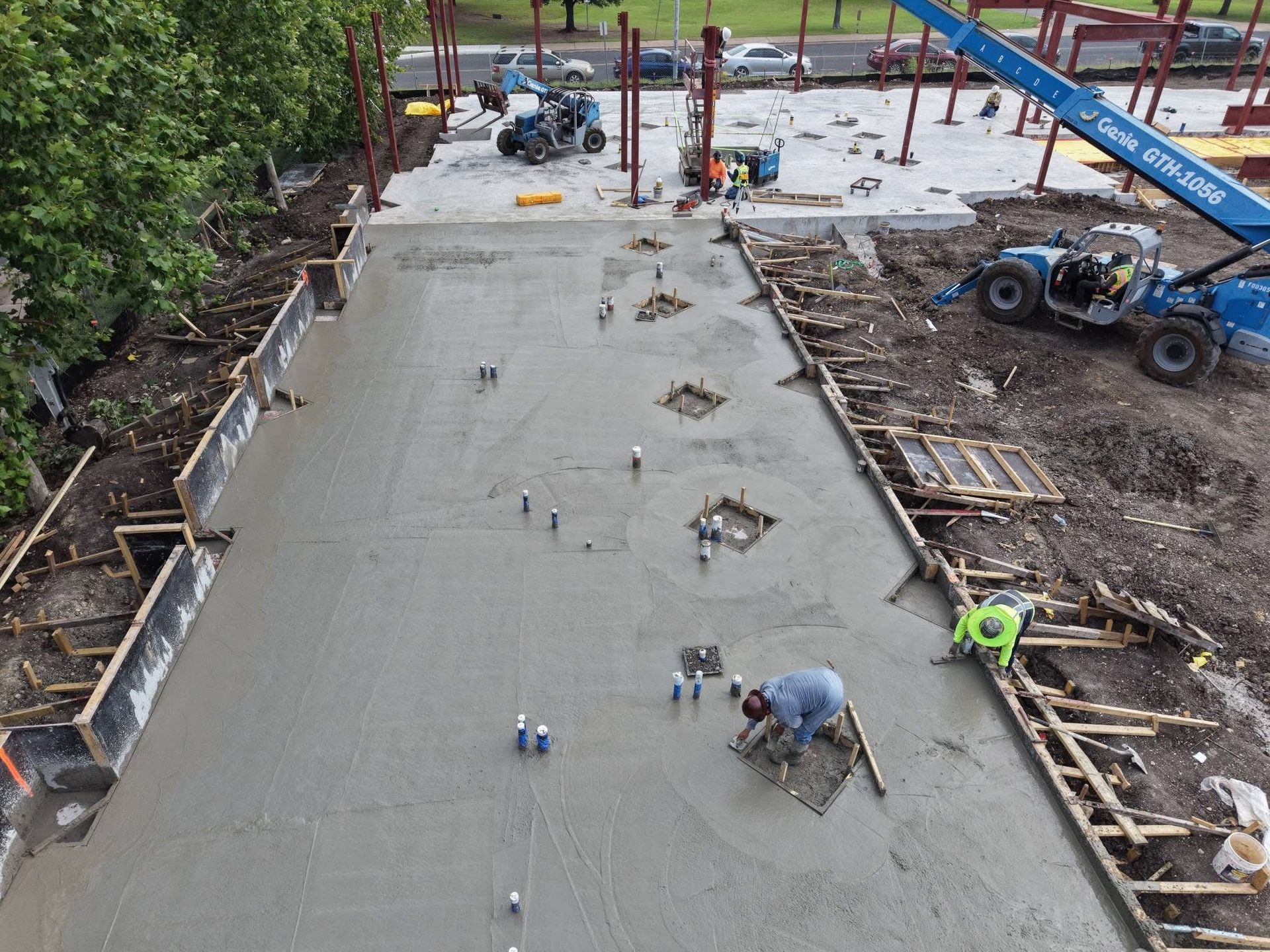 Workers smoothing fresh concrete on a large construction slab with heavy equipment nearby